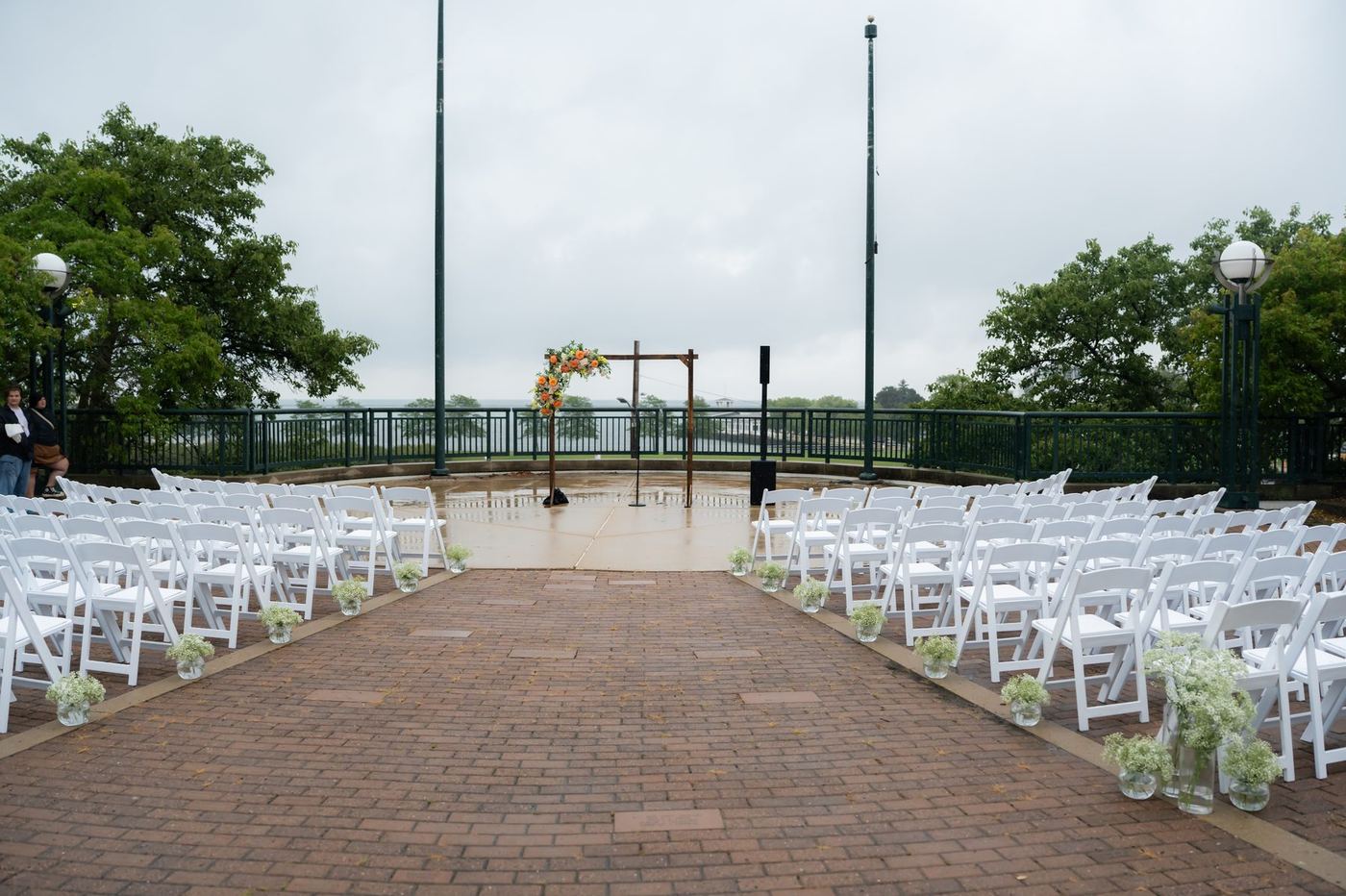 Outdoor ceremony seating with a floral arch on a rainy waterfront terrace