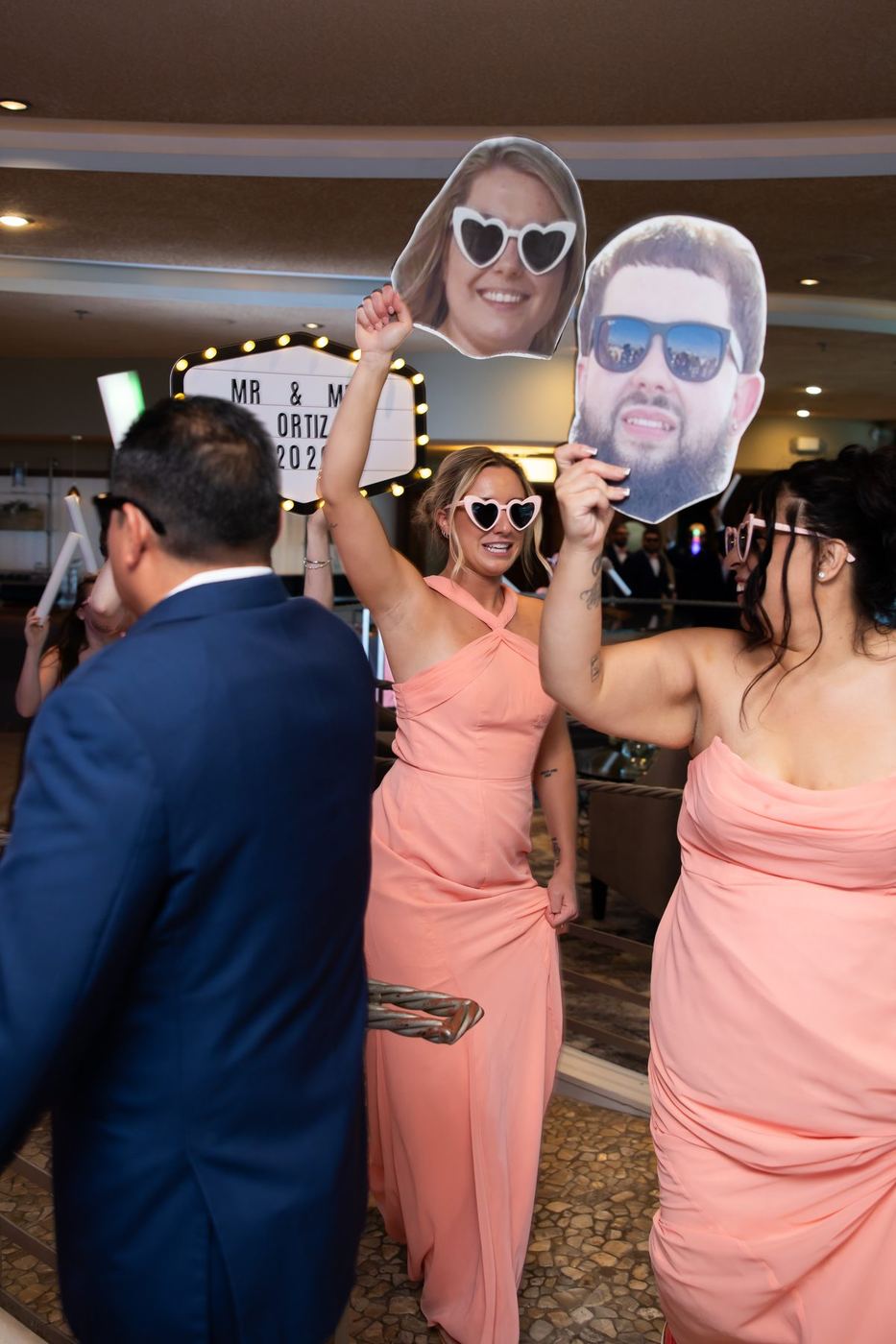 Wedding party in coral dresses holding oversized photo cutouts